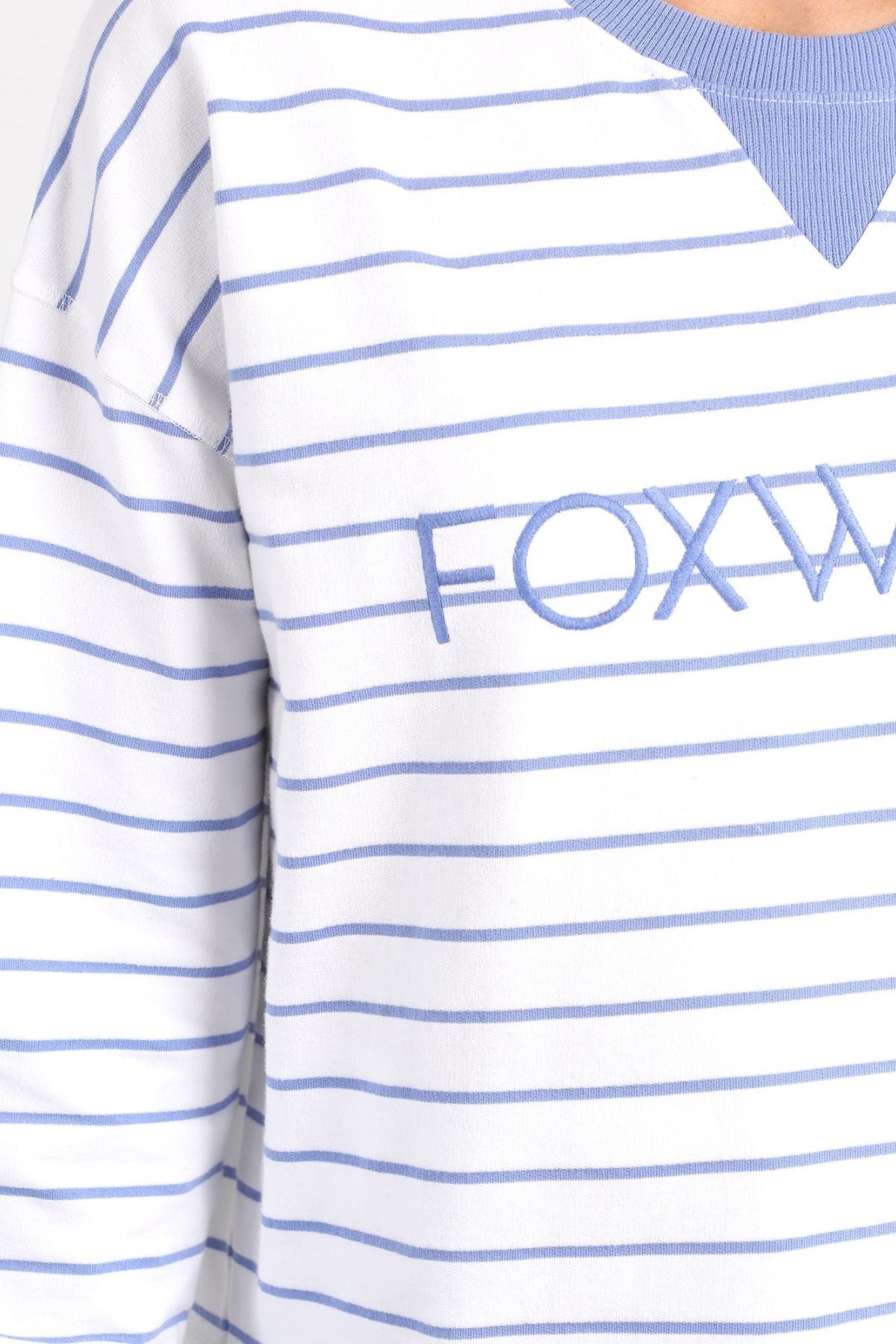 Close-up of a person wearing the Foxwood Simplified Stripe Crew, a white and blue striped shirt featuring "FOXW" embroidery in blue. The partially visible neckline highlights the comfortable 100% cotton material.