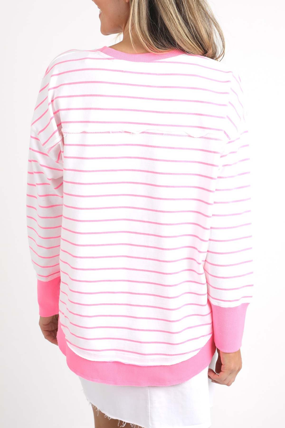 A person with long hair is wearing a Foxwood Simplified Stripe Crew sweater, known for its relaxed fit and crafted from 100% cotton. The sweater features pink stripes and cuffs, viewed from the back, paired with a white skirt against a plain white background.