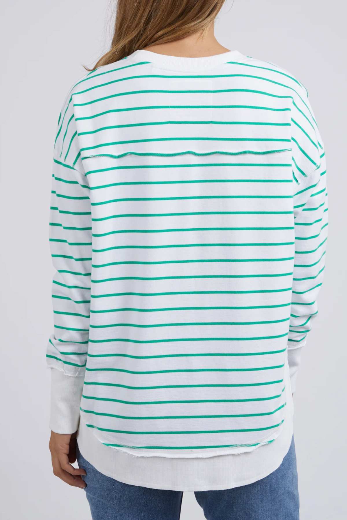 A person with light brown hair is seen from the back wearing blue jeans and a Foxwood Simplified Stripe Crew—white with green stripes, 100% cotton, relaxed fit.