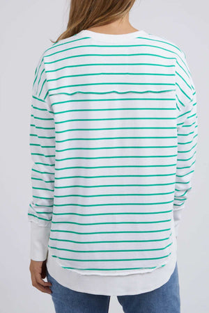 A person with light brown hair is seen from the back wearing blue jeans and a Foxwood Simplified Stripe Crew—white with green stripes, 100% cotton, relaxed fit.