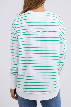A person is seen from the back wearing the Foxwood Simplified Stripe Crew, a relaxed-fit sweater made of 100% cotton. It features white and green horizontal stripes, long sleeves, and a straight hem, paired with blue jeans. Brown hair flows over their shoulders against a plain white background.