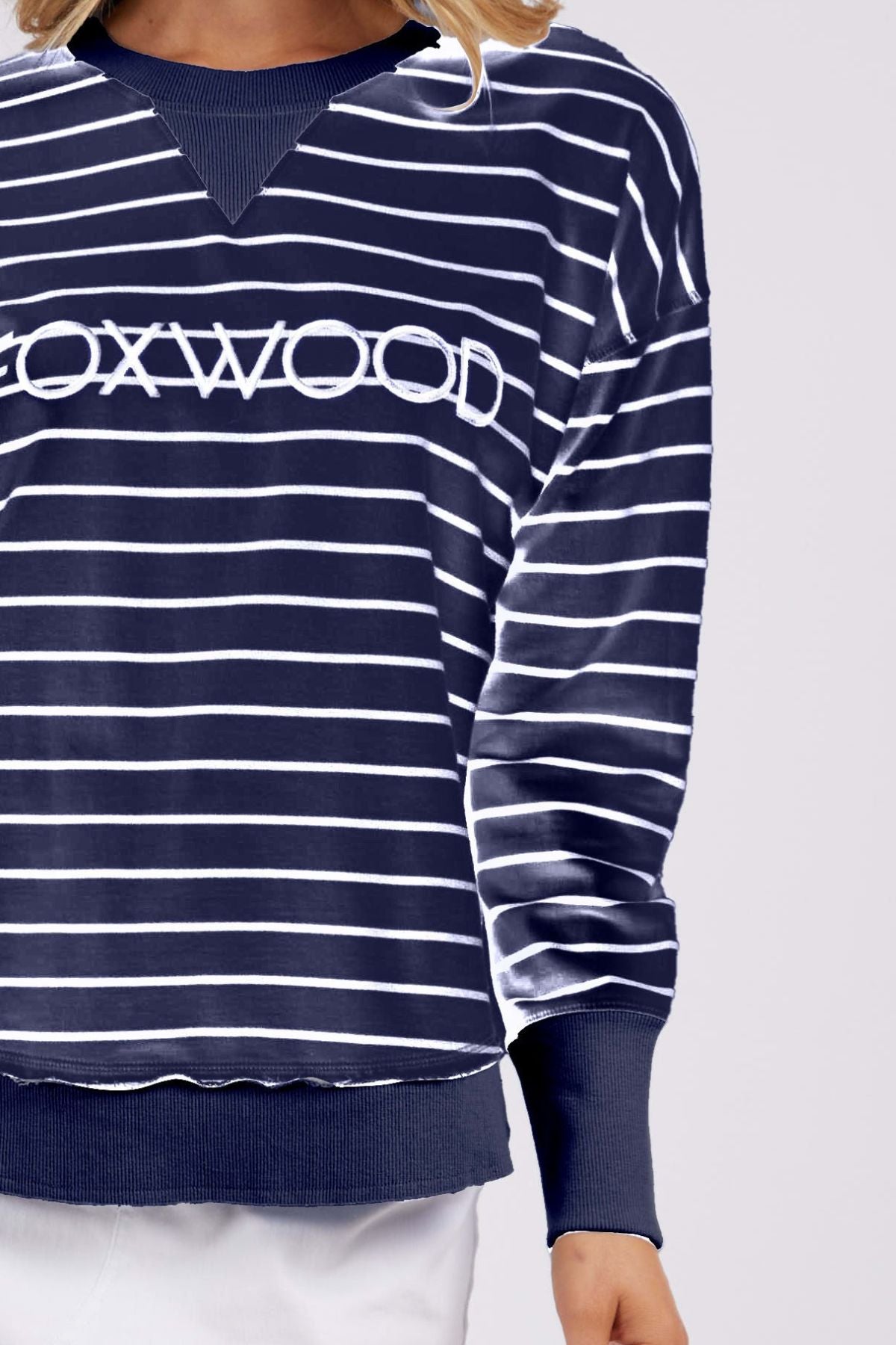 A person is wearing a Foxwood Classic Stripe Simplified Crew sweater in navy blue and white stripes, made from 100% cotton. The sweater boasts a relaxed fit with long sleeves, a ribbed hem, and the word "BOXWOOD" prominently displayed across the front. They pose against a plain backdrop, partially concealing their face.