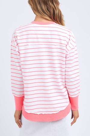 A person with long hair is wearing the Foxwood Simplified Stripe Crew, a white and pink striped sweater from Foxwood Clothing. Ideal for layering, its long sleeves and relaxed fit allow it to drape casually as they face away from the camera against a plain white background.