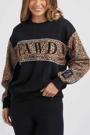 A person wearing the Foxwood The Panel Crew, which is a stylish black sweatshirt featuring "AIVD" embroidered on the chest and bold animal print panels adorning the sleeves. Their wavy, shoulder-length hair frames their face as they exude confidence, posing with one hand resting on their hip.