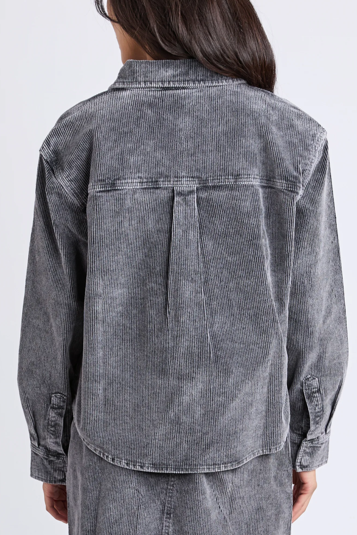 A person with long, dark hair is seen from behind wearing the Foxwood Tularose Cord Shirt, a relaxed-fit gray corduroy shirt with buttoned cuffs, a back box pleat, and a subtle striped texture for effortless style.