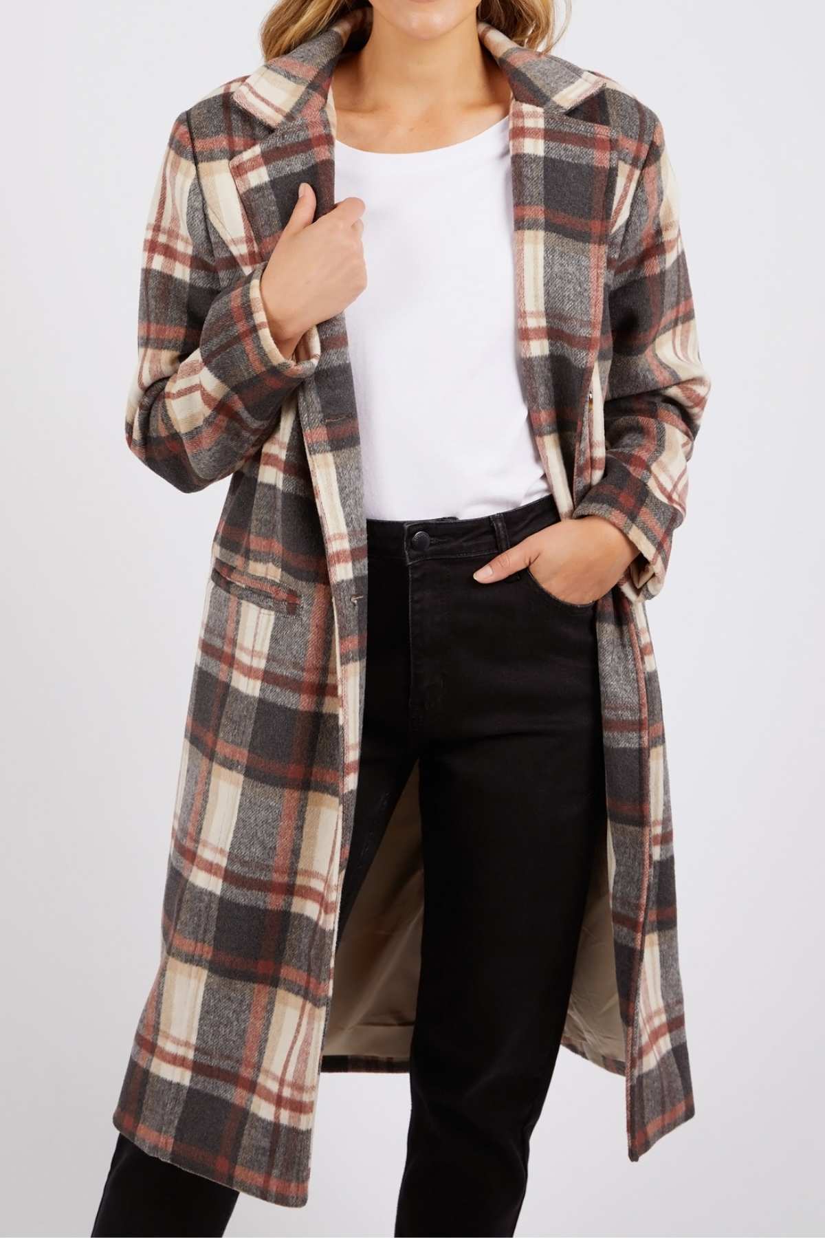 Wearing the Foxwood Westward Coat, a yarn-dyed check in brown, beige, and white, over a white shirt and black pants; standing with one hand in their pocket and the other holding the coat lapel.
