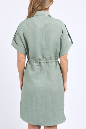 A woman with loose light brown hair faces away, wearing the Foxwood Willow Shirt Dress. This sage green linen-viscose blend dress has a drawstring waist and folded cuffs, set against a plain white background.