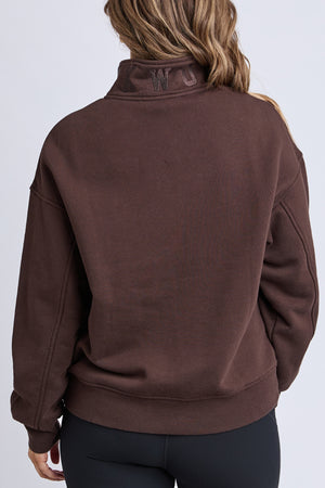 A person with wavy brown hair, seen from the back against a plain light background, wears the Foxwood College Zip Crew featuring "WC" embroidery on the high zip neck, paired with black leggings.