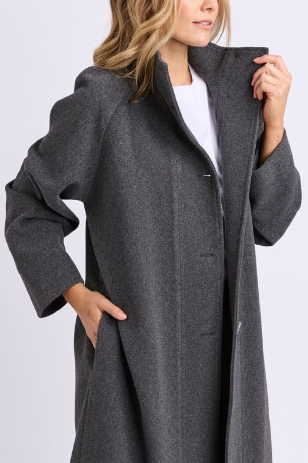 A woman in the Foxwood Fermont Coat, ideal as a transitional jacket, stands with one hand in her pocket and the other on the lapel. Her loose waves frame her partially visible face.