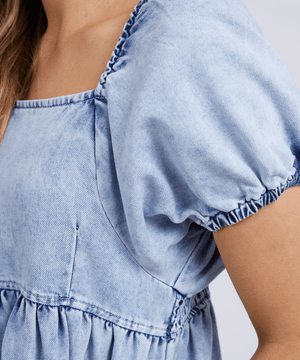 Close-up of someone wearing the Foxwood Jade Textured Dress, a light blue cotton dress with short sleeves and gathered stitching at the sleeves and waist. The person's face is not shown.