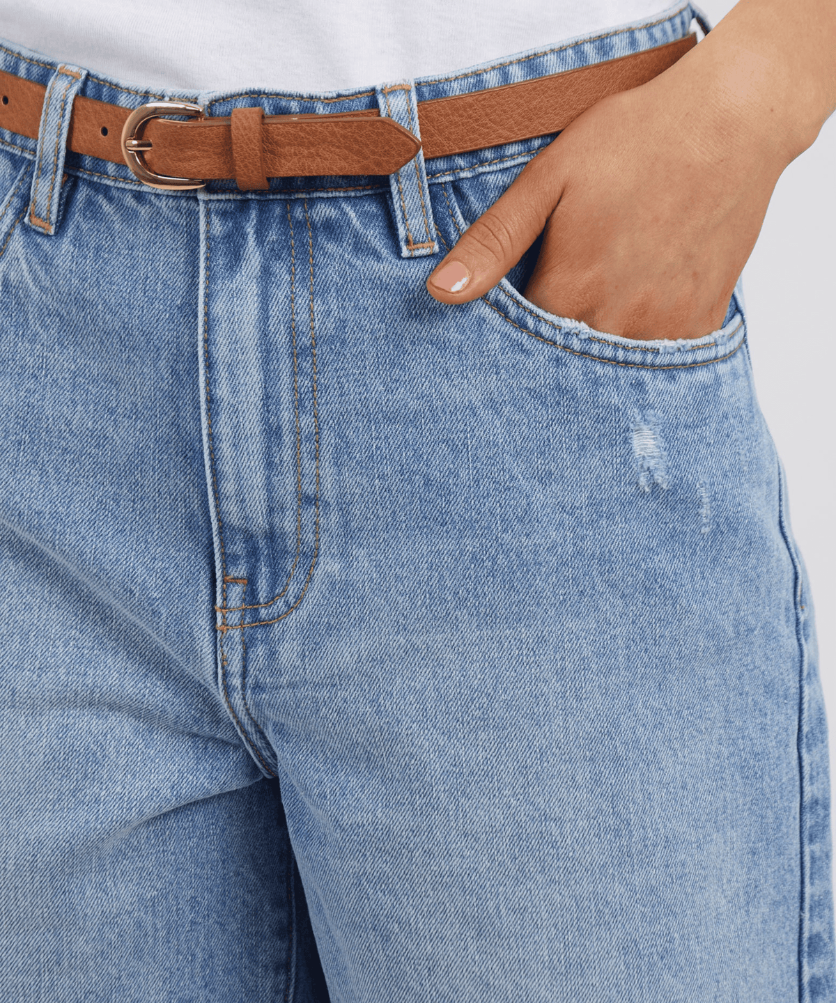 Wearing the Foxwood Millie Short in light blue with a brown belt and white shirt, one hand in the pocket, creates a relaxed vibe akin to classic frayed-hem denim shorts.