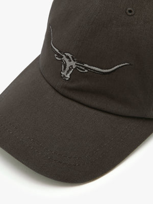 A close-up of the RM Williams Longhorn Cap in dark brown cotton twill, showcasing an embroidered longhorn skull logo on the front.