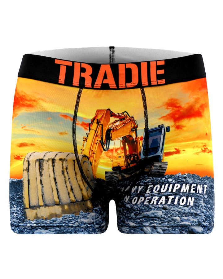 The Tradie Mens Work N Surf Trunk features a bold print of a yellow excavator and bulldozer against an orange sunset, moisture-wicking quick-dry fabric, and an orange "TRADIE" waistband.