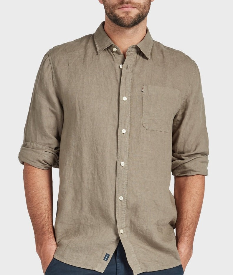 A man wears the Academy Brand Hampton Linen Shirt in light brown with rolled-up sleeves, hands in pockets, and a visible chest pocket against a plain light background.