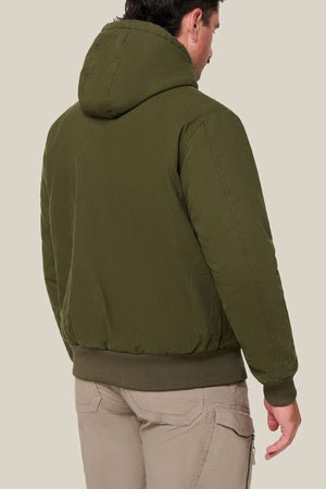 A man faces away, wearing the Hard Yakka Canvas Bomber Jacket in olive green and light beige cargo pants against a plain light background.