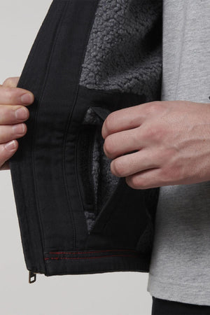A person opens the side of a Hard Yakka Heritage Canvas Hooded Jacket, exposing a soft sherpa fleece lining. Their other hand grips near the pocket with its heavy-duty zip, while wearing a light gray shirt.