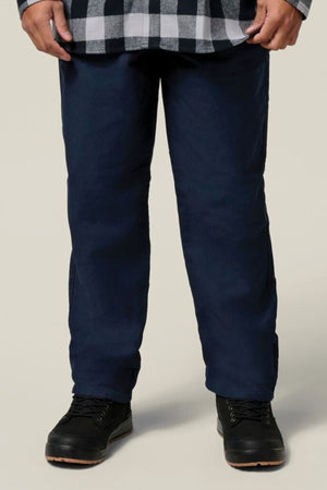 A person wearing black and white plaid, the Hard Yakka Moleskin Plain Front Heavy Duty Work Pant, and black lace-up shoes stands against a plain light background; only their lower half is visible.