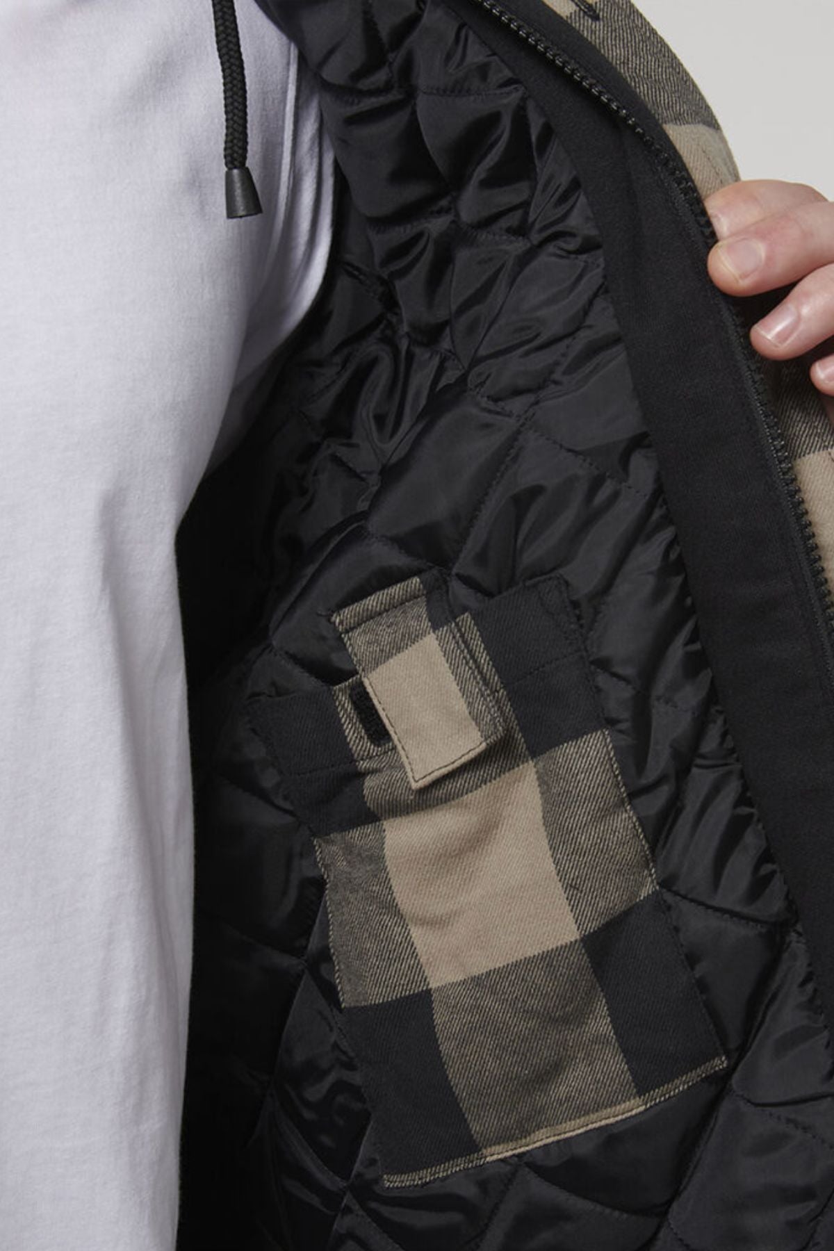 Close-up of a person holding open a black Hard Yakka Quilted Flannelette Shacket to reveal the interior. The interior features a pocket with a plaid pattern in beige and black. The comfortable shacket fits perfectly over the white shirt they're wearing.