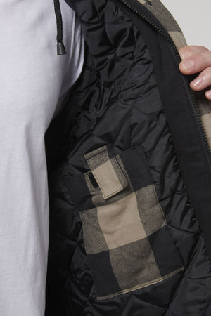 Close-up of a person holding open a black Hard Yakka Quilted Flannelette Shacket to reveal the interior. The interior features a pocket with a plaid pattern in beige and black. The comfortable shacket fits perfectly over the white shirt they're wearing.