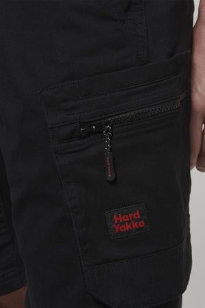 Close-up of a person wearing the Hard Yakka Tough Maxx Mid Short, featuring visible stitching, a zippered pocket, UPF 50+ protection, and a red Hard Yakka logo patch above the pocket.