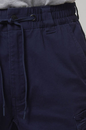 Close-up of a person wearing Hard Yakka Tough Maxx Mid Short navy pants with an elastic waistband, belt loops, and drawstring, paired with a tucked-in light gray shirt. The fabric is comfortable and provides UPF 50+ protection for daily wear.