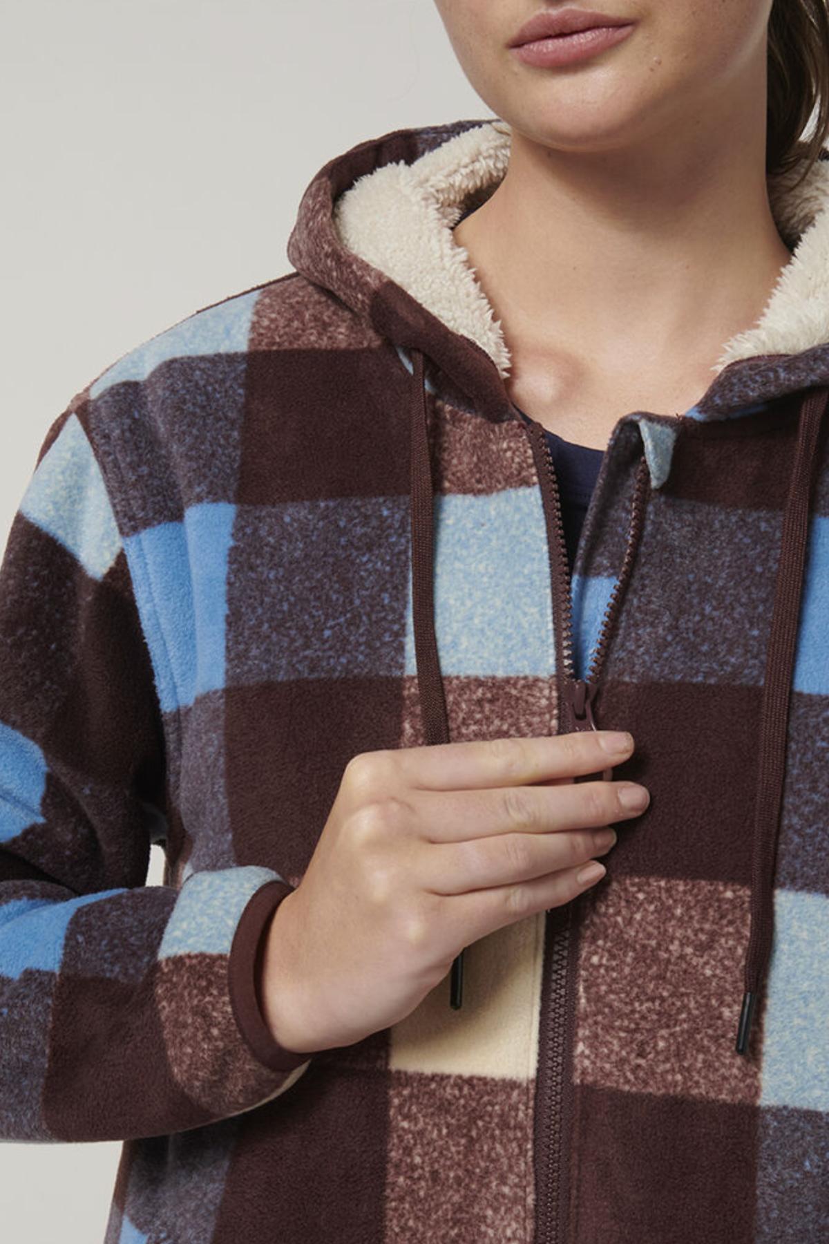 A woman in the Hard Yakka Womens Check Zoodie, showcasing a blue, brown, and cream plaid design with a fleece body and sherpa-lined hood for warmth. Only her lower face and upper torso are visible as she holds the zipper.