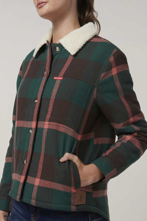 A person wears the Hard Yakka Womens Heritage Trucker Sherpa Jacket, featuring green, brown, and red plaid, a white sherpa collar, snap buttons, a small red chest label, regular fit, with one hand in a pocket.