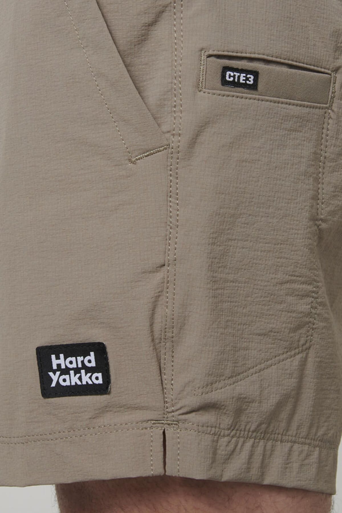 A close-up of the beige Hard Yakka X Short Short features two patches: "Hard Yakka" near the hem and "CTE3" above the pocket. These shorts are made from durable Cordura Nylon with 4-way stretch for unparalleled comfort.