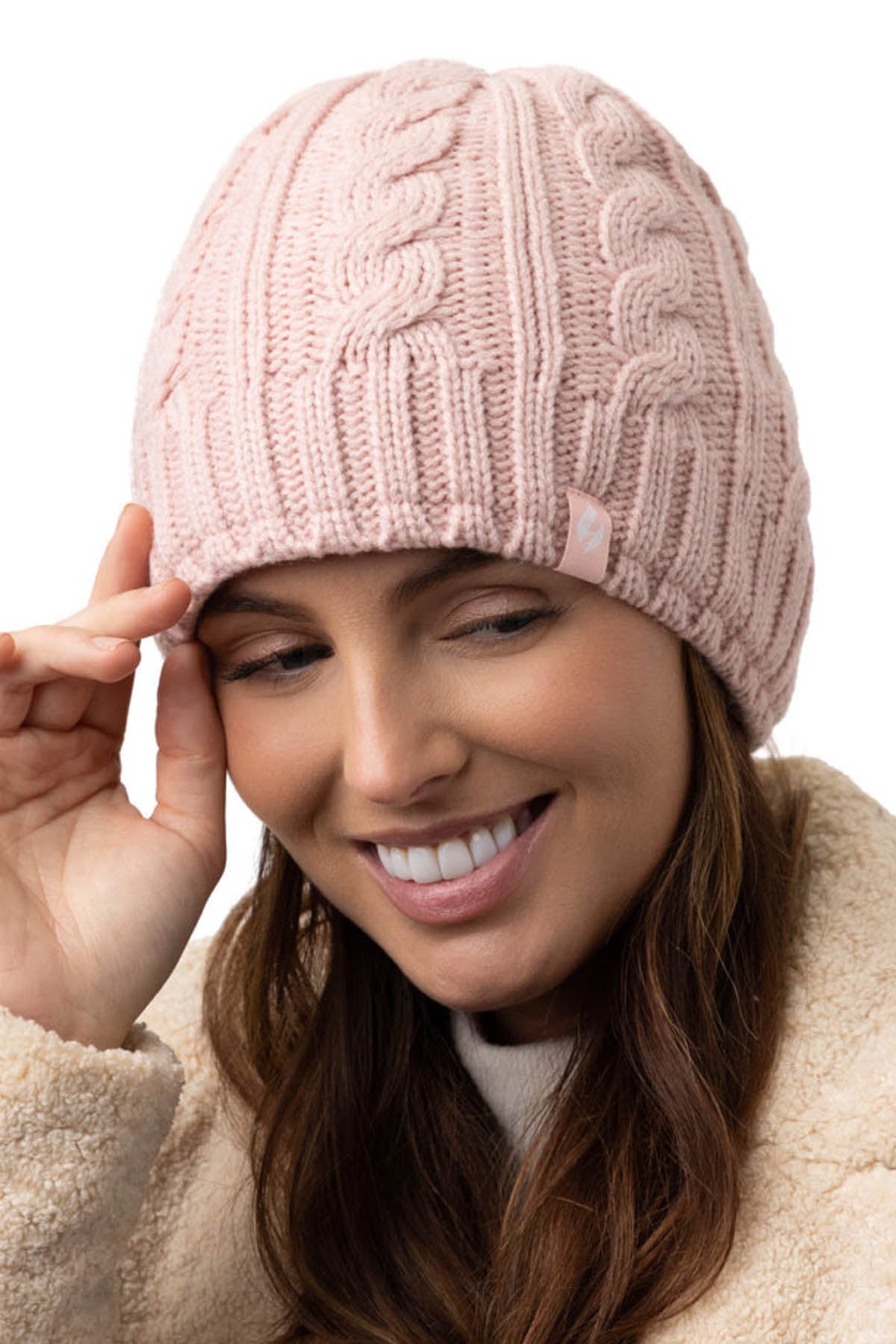 A person wearing a pink Heat Holders Alesund Ladies Thermal Beanie and a beige fuzzy jacket smiles while tilting the beanie slightly with their right hand. The background is white.