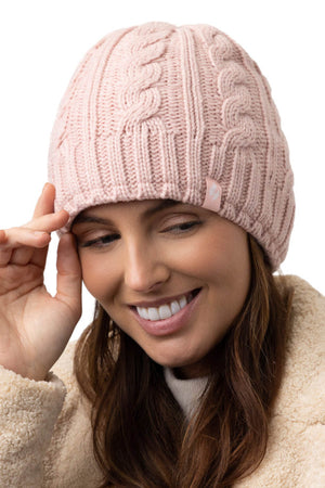 A person wearing a pink Heat Holders Alesund Ladies Thermal Beanie and a beige fuzzy jacket smiles while tilting the beanie slightly with their right hand. The background is white.