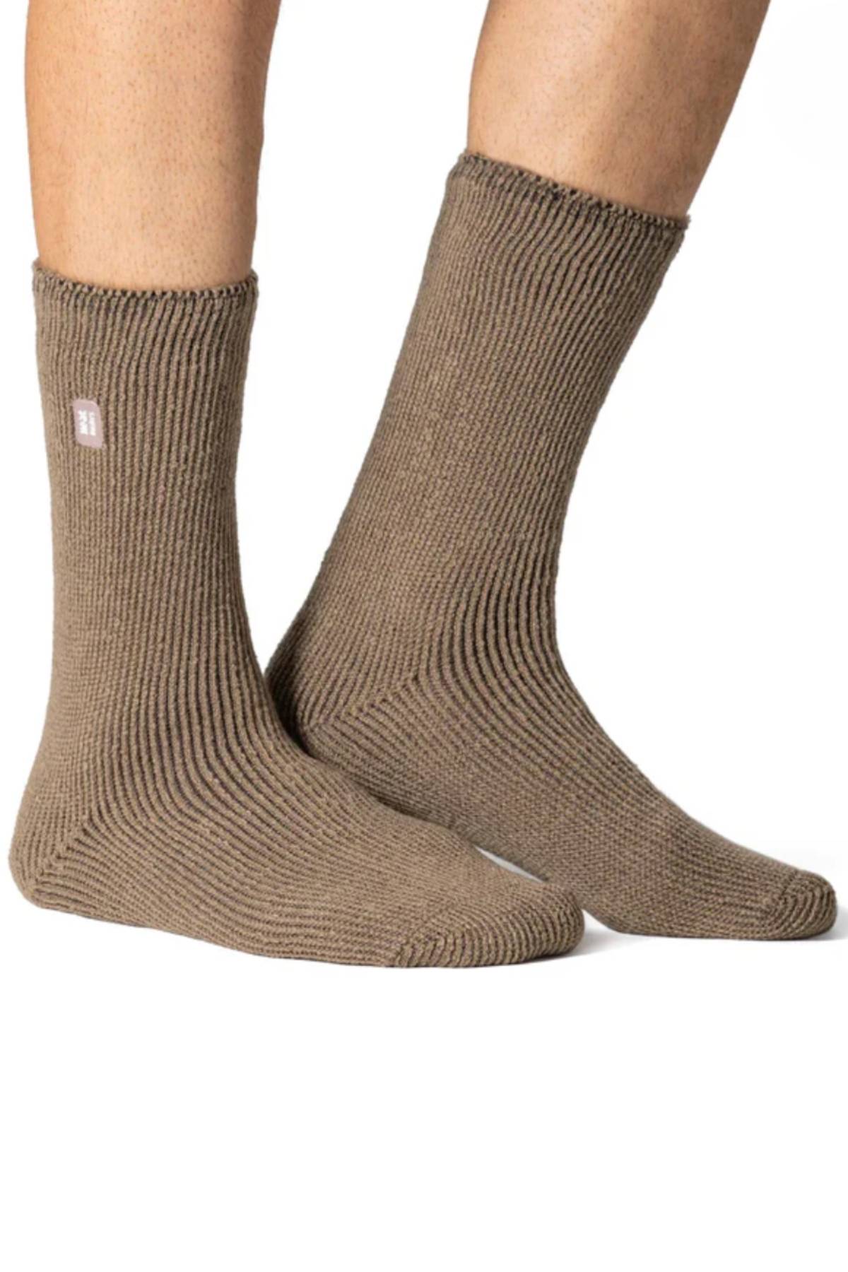 A pair of feet wear light brown Original Thermal Heat Holders Socks against a white background. These ribbed, mid-calf socks offer long pile cushioning for comfort and feature a small rectangular label near the top.