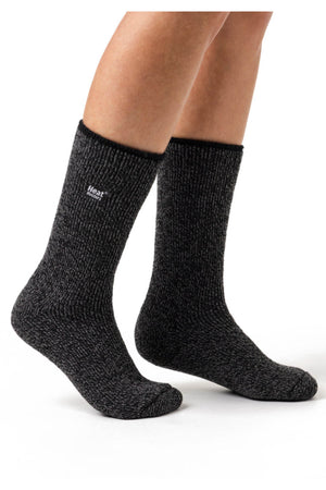 Two legs wearing dark grey, thick, knitted Heat Holders Ladies Wool Socks standing on a white background. Made with Merino wool for added comfort and boasting an impressive TOG rating, these socks appear to be cozy and suitable for keeping feet warm.