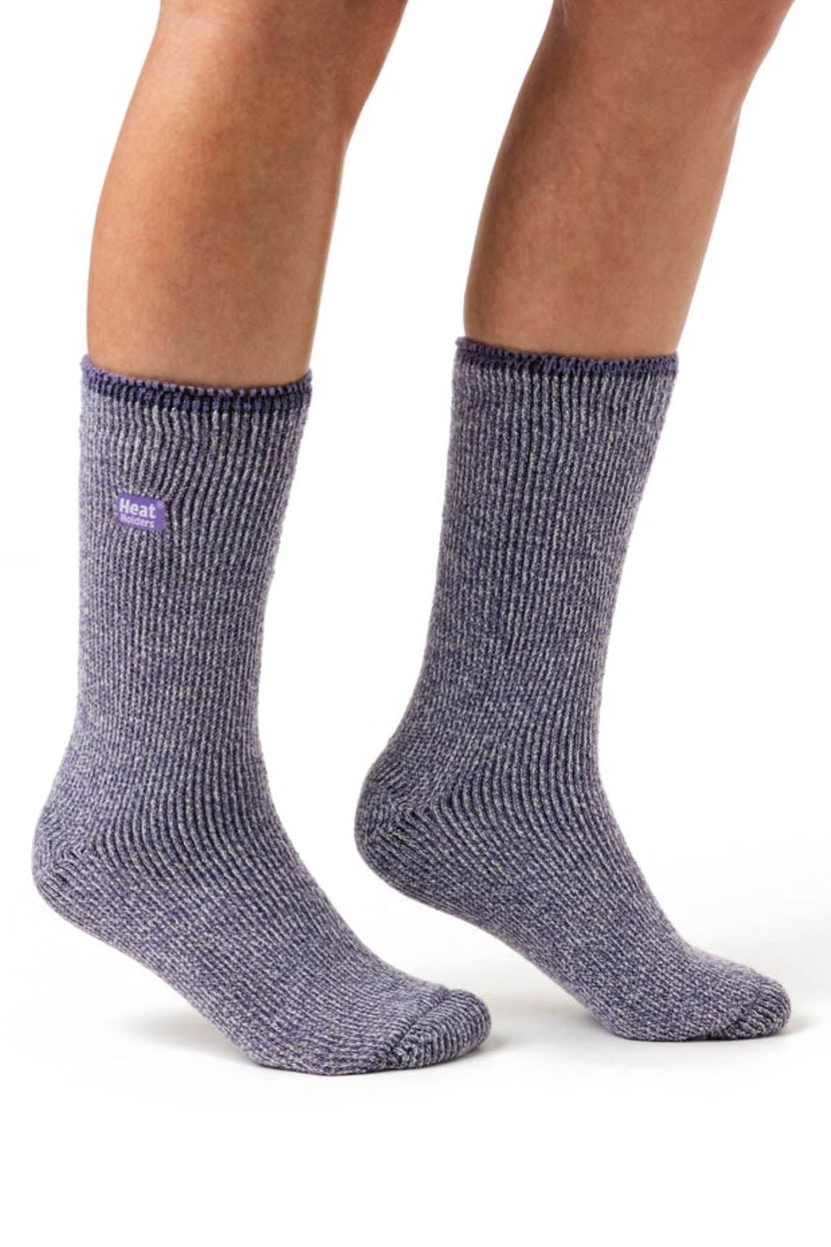 A pair of feet wearing Heat Holders Ladies Wool Socks made from gray thermal Merino Wool with a textured, ribbed knit. The socks rise to mid-calf and have a small purple tag near the top. Known for their exceptional warmth and comfort, these socks are perfect for outdoor activities. The feet are standing on a white, seamless background.