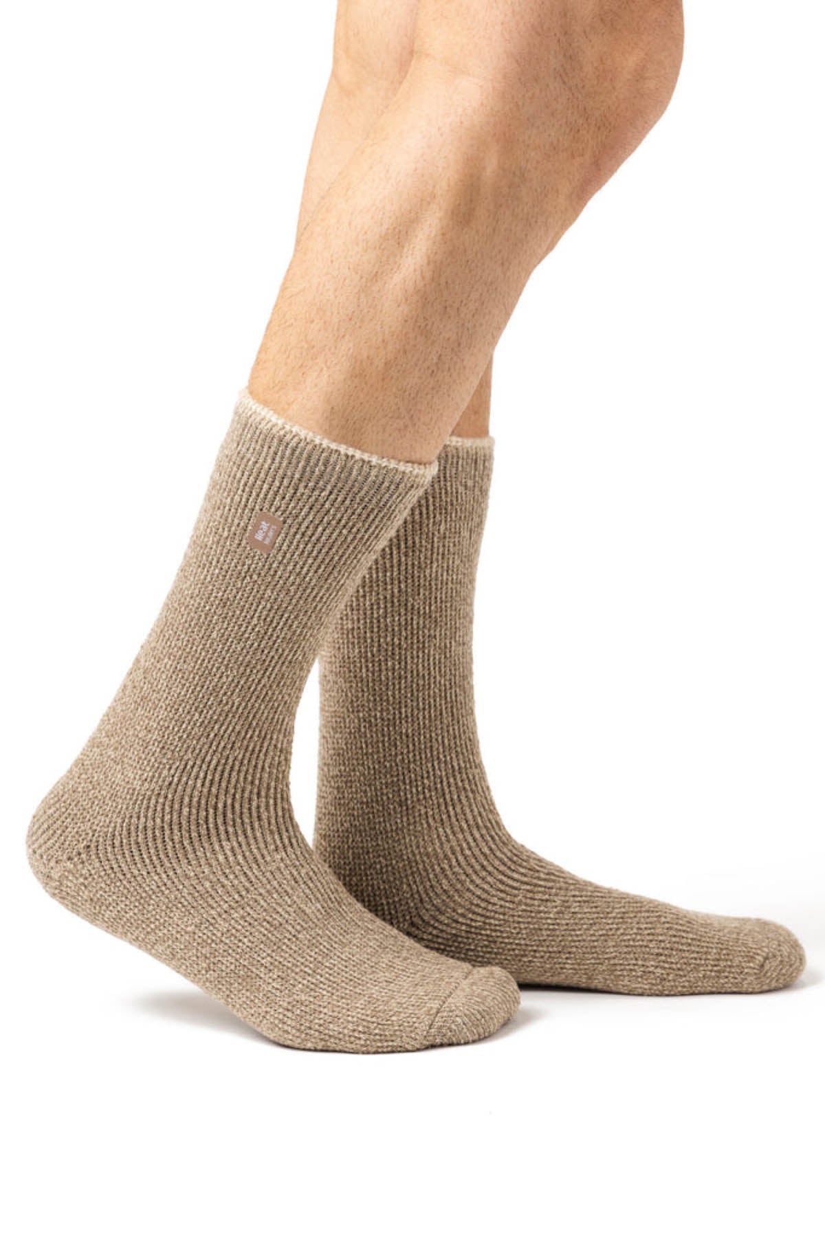 Against a white backdrop, someone wears beige ribbed knit socks akin to Heat Holders Mens Wool Sock, known for superior warmth. A small emblem is visible near the top of the socks. With only their legs shown, they seem ready for an outdoor adventure.