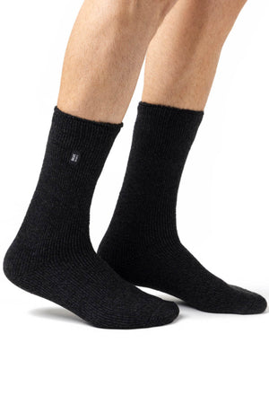 A picture of a person wearing the Original Thermal Heat Holders Sock, which are dark gray, ribbed, and mid-calf in length, designed specifically for cold weather. Only the legs and feet are visible against a white background. These warm socks feature a small black tag with white text near the top, underscoring their superior warmth and comfort.