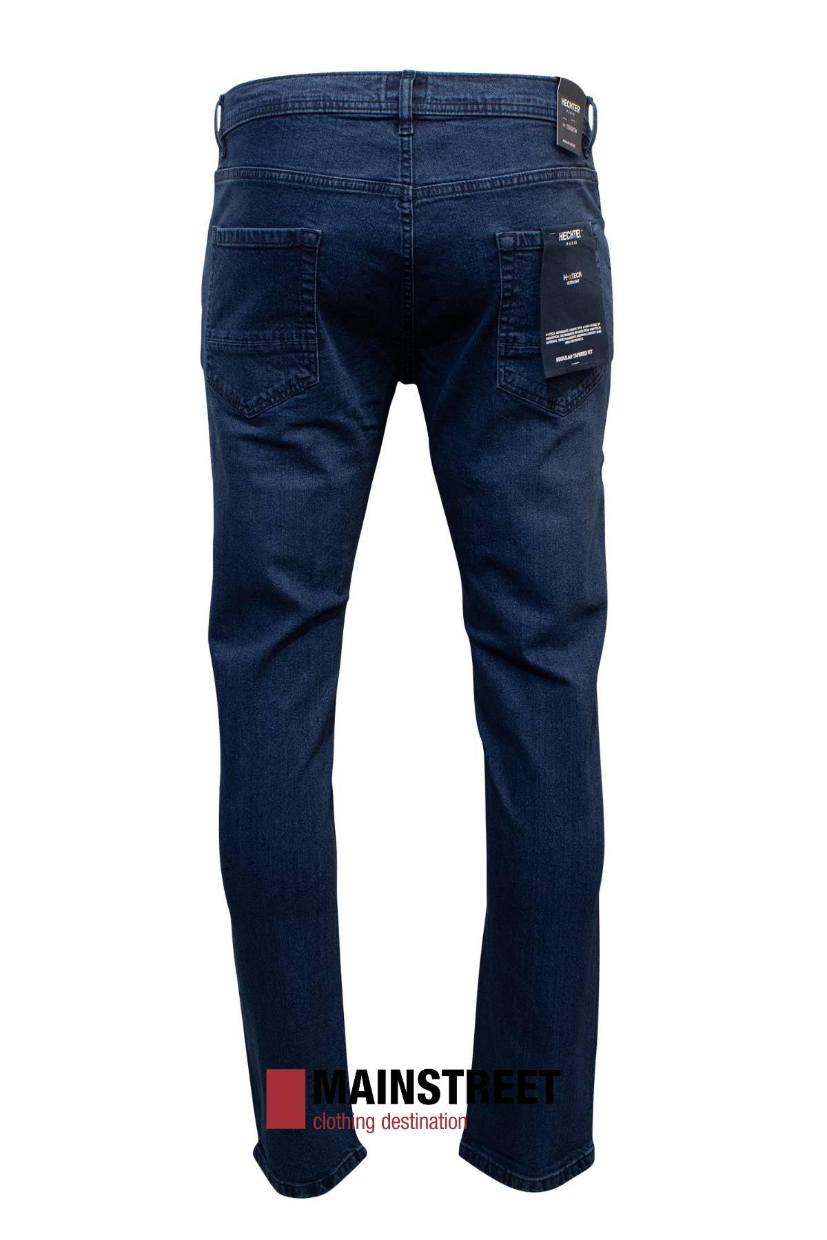 Back view of Hechter Dallas Stretch Jean in dark blue denim with visible stitching and branded back pocket tags. Crafted from cotton and elastane, these jeans offer a regular tapered fit. Shown on a white background with the MAINSTREET logo.