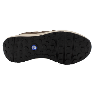 The image shows the sole of a Florsheim Excursion Slip On shoe with a rugged, textured pattern for shock absorption, featuring hexagonal grips and a small blue logo in the center. The sole is primarily black with brown detailing along the edges.