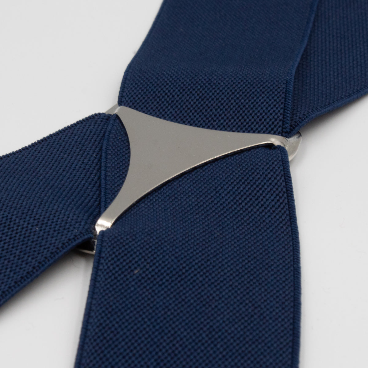 A close-up of Buckle Plain Braces shows a blue fabric strap intricately woven with a shiny metal connector in an x-back shape. The fabric's texture contrasts with the smooth metal, and high-quality clasps ensure durability against the plain white background.