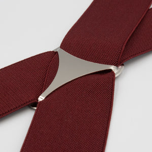 Close-up of the Buckle Plain Braces, a stylish maroon woven fabric belt featuring a sleek silver metallic buckle and high-quality clasps, displayed on a flat surface to accentuate its texture and elegant design.