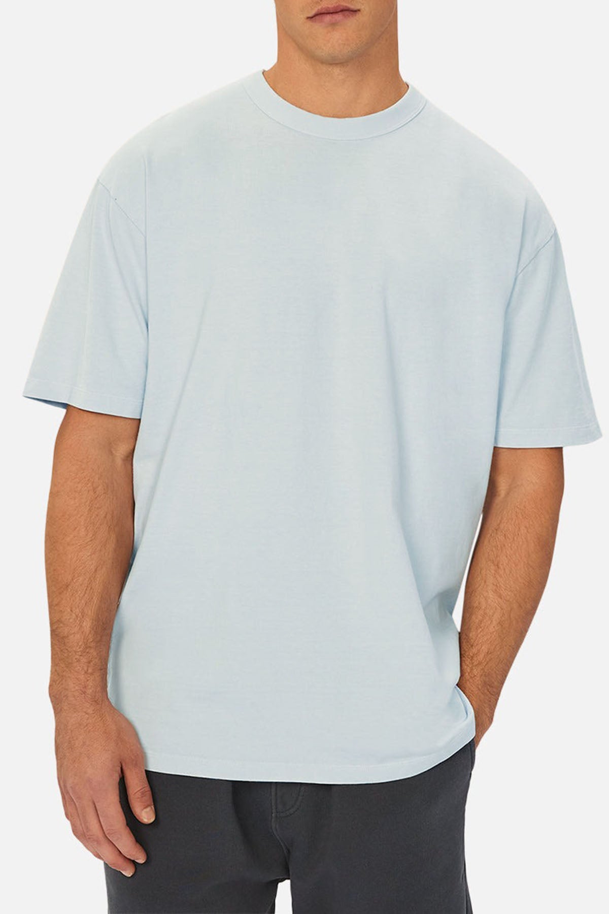 A man models the Industrie The Del Sur Tee in light blue with short sleeves and dark pants, standing against a plain white background—ideal for showcasing chest measurements in a size guide.