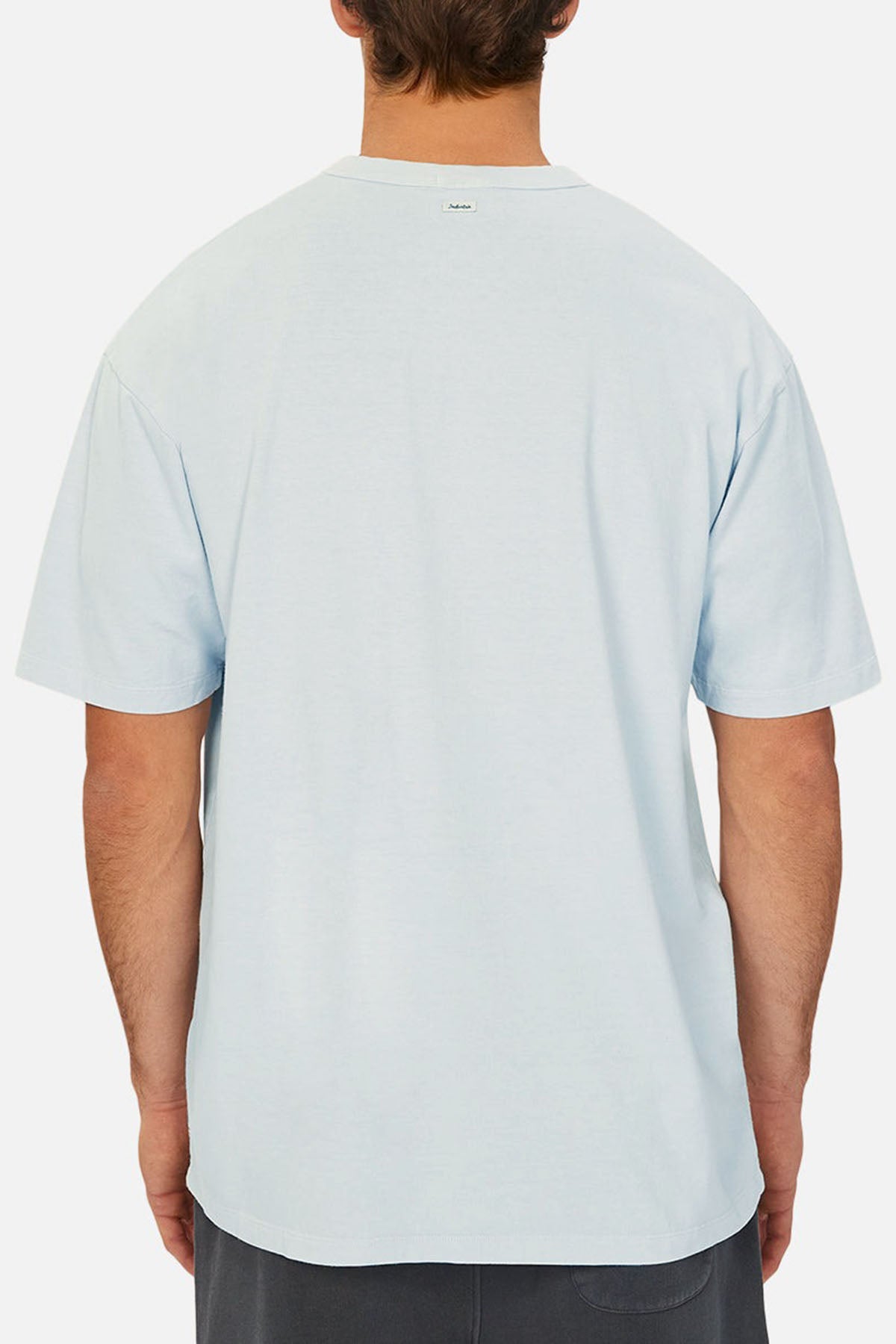 A person with short brown hair is shown from the back wearing the Industrie The Del Sur Tee, a loose-fitting light blue short-sleeve shirt, and dark shorts against a plain white background—ideal for referencing chest measurement or size guide.