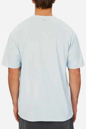 A person with short brown hair is shown from the back wearing the Industrie The Del Sur Tee, a loose-fitting light blue short-sleeve shirt, and dark shorts against a plain white background—ideal for referencing chest measurement or size guide.