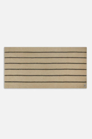 The Industrie The Comporta Beach Towel, a rectangular beige towel with evenly spaced thin black horizontal lines in a halo stripe design, is displayed on a plain white background.