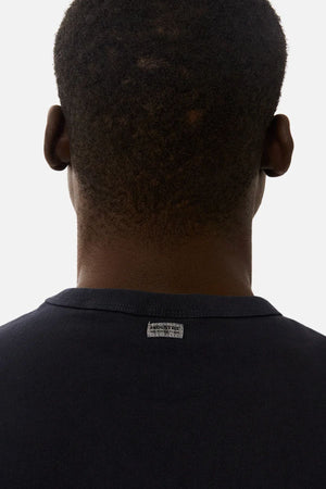 A close-up of the back of a person’s head and neck, showing short dark hair. They are wearing the Industrie The Del Sur Sleeveless Tee, featuring a small rectangular label on the back collar.