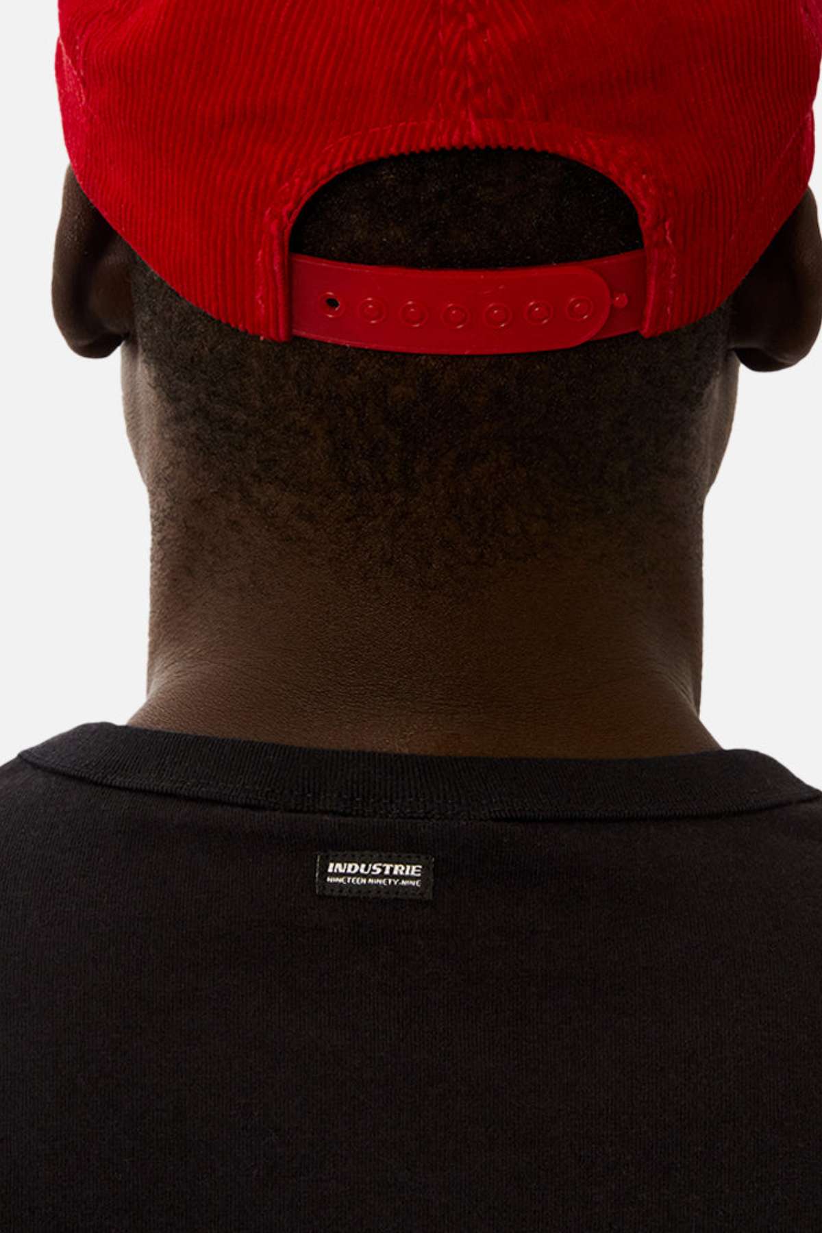 A person is seen from behind wearing a red backwards baseball cap and the Industrie The Del Sur Sleeveless Tee, an oversized black shirt with a small "INDUSTRIE" label near the collar.