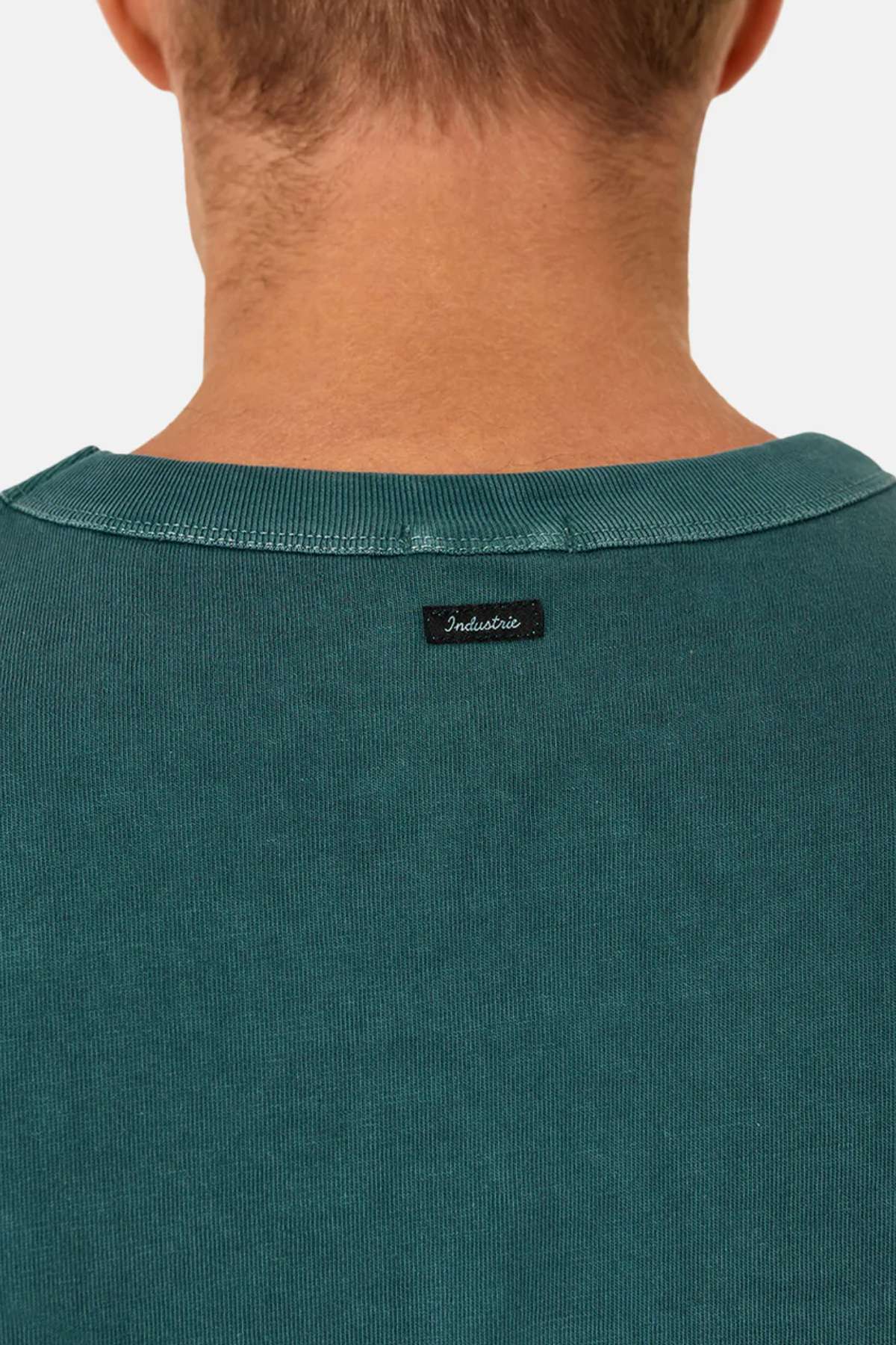 Close-up of the back of a person’s neck and shoulders wearing the Industrie The Del Sur Tee, a teal ribbed 100% cotton shirt with a small black “Industrie” tag sewn at the neckline.
