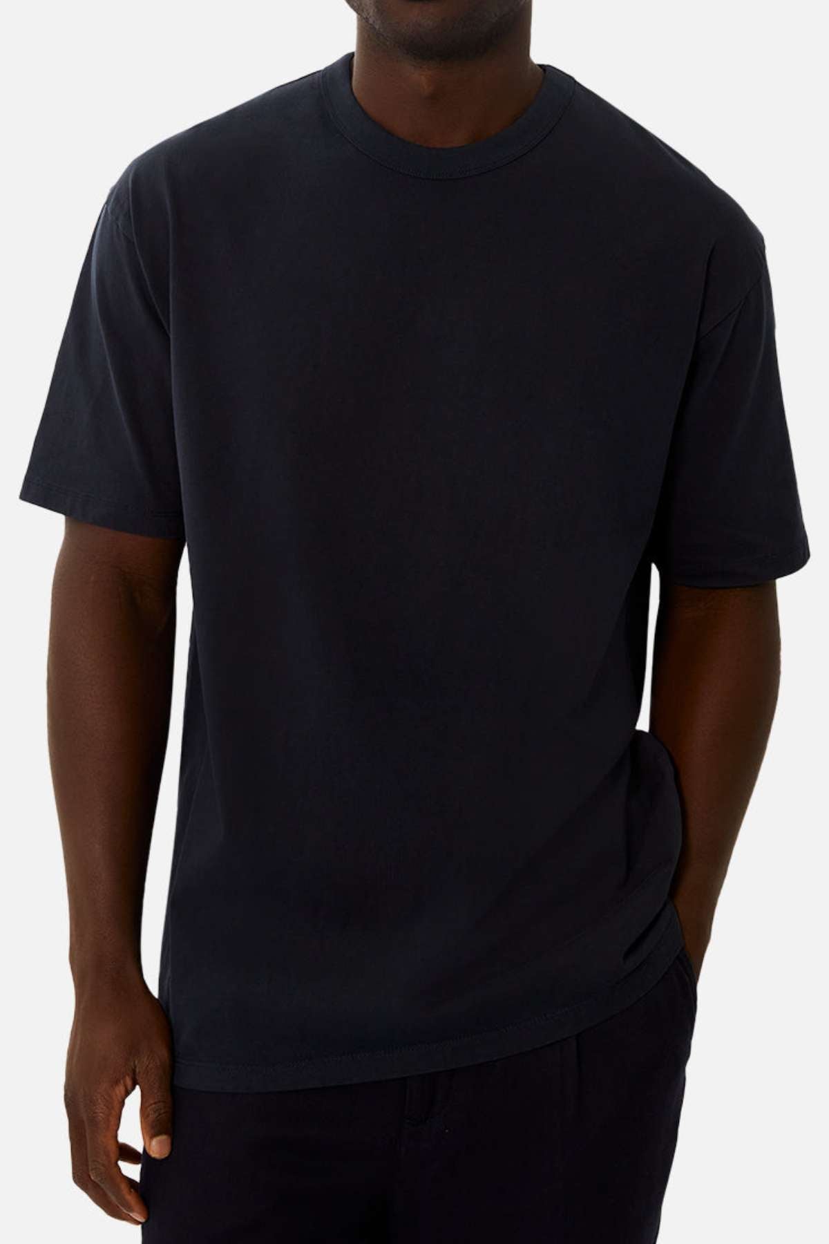 A person models the Industrie The Del Sur Tee—an oversized acid wash shirt—paired with dark pants, standing against a light background with one hand in their pocket. Their face is partially obscured.