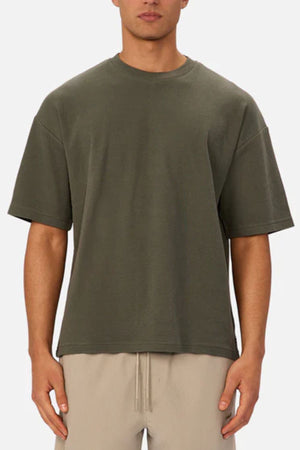 A man wearing the Industrie The Marlon Tee in dark olive green and light beige drawstring pants, perfect for casual wear, stands against a plain light background.