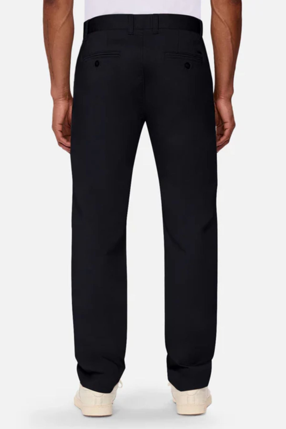 A person stands facing away from the camera in Industrie The Regular Cuba Chino Pant, a stretch cotton blend with a wide leg fit, belt loops, and two buttoned back pockets, paired with a white shirt and white sneakers.
