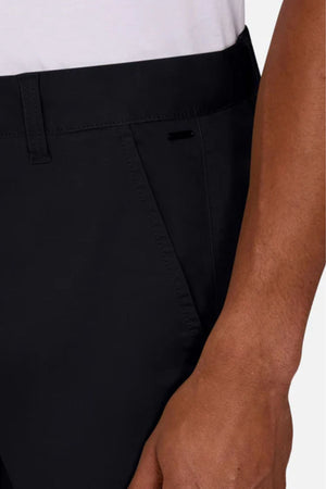 A close-up of a person wearing Industrie The Regular Cuba Chino Pant in black stretch cotton, highlighting the waistband, pocket, and part of their right hand and arm against a plain background.
